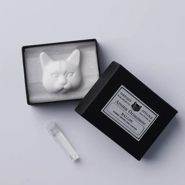 A white oil diffuser in the shape of a cat's head, displayed next to its black packaging box with a label.