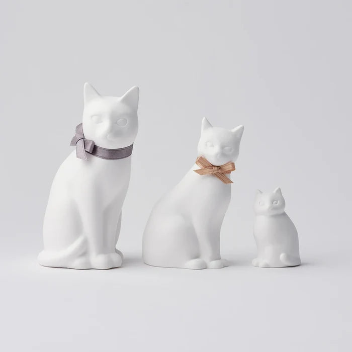 A set of three white cat-shaped oil diffusers, each with different sizes and adorned with different colored bows.