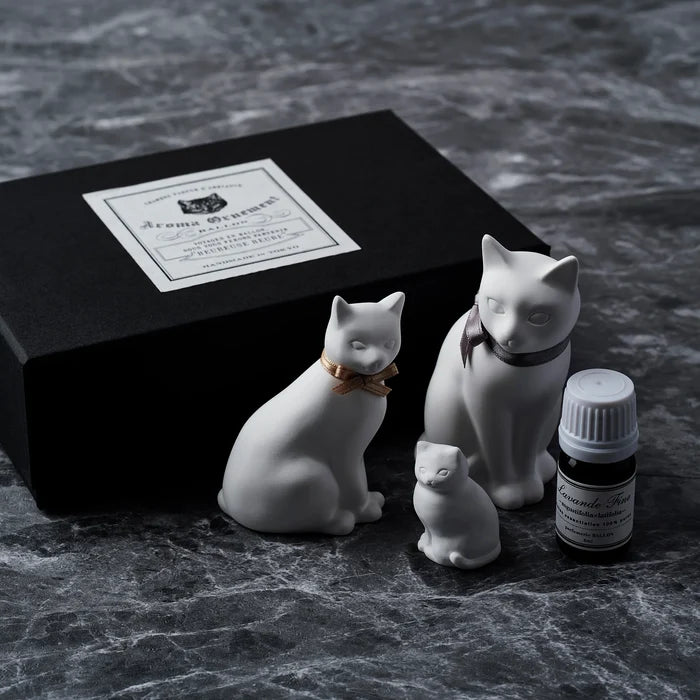 White cat-shaped aroma ornament set with large and small ceramic cat figures, essential oil bottle, and black gift box, displayed on a dark marble surface in a minimalist home fragrance product scene.