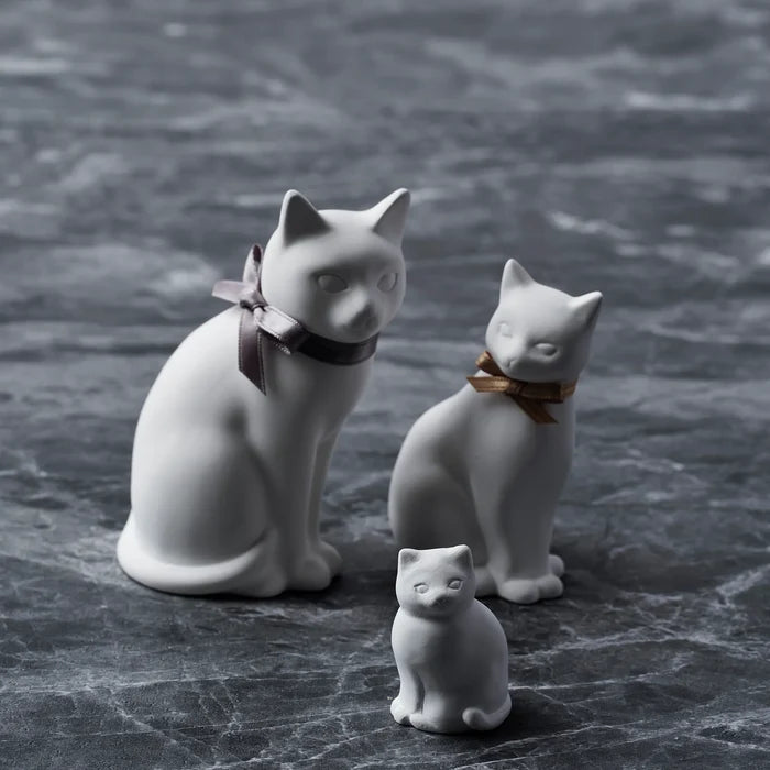 Set of white cat-shaped aroma ornaments in three sizes, displayed on a dark marble surface with ribbon collars in a minimalist home decor product scene.
