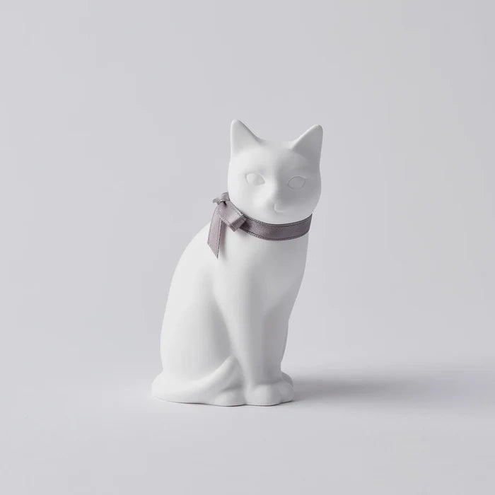A white oil diffuser in the shape of a cat with a bow around its neck.