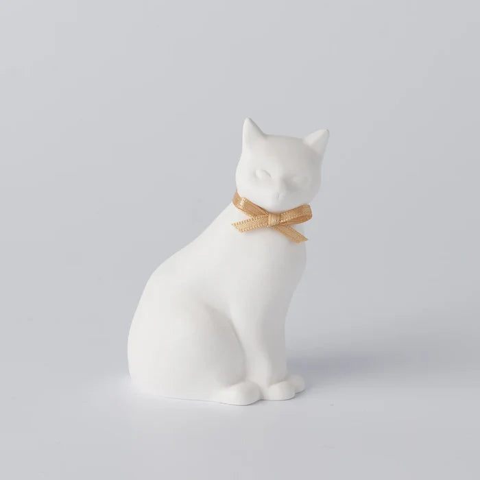 A white ceramic oil diffuser in the shape of a cat with a small bow tie.