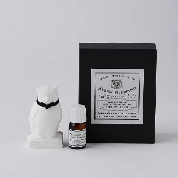 White owl-shaped aroma ornament gift set with a black ribbon collar, essential oil bottle, and black vintage-style box, displayed on a clean white background in a minimalist home fragrance product presentation.