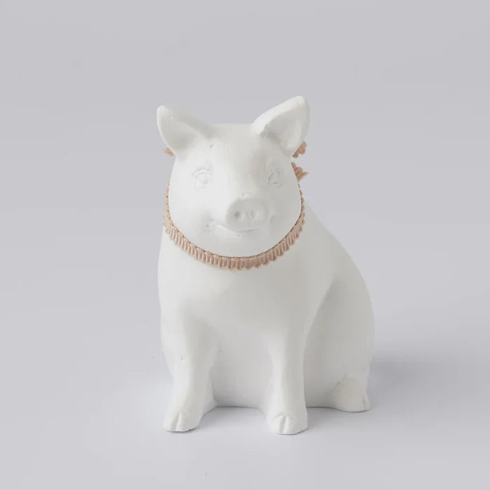 A white ceramic oil diffuser in the shape of a pig with a decorative collar.