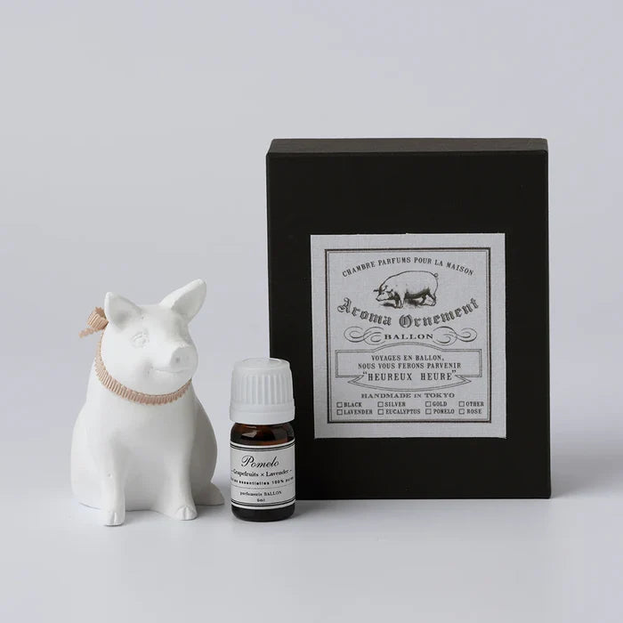 White pig-shaped aroma ornament gift set with a ribbon collar, essential oil bottle, and black vintage-style box, displayed on a clean white background in a minimalist home fragrance product presentation.