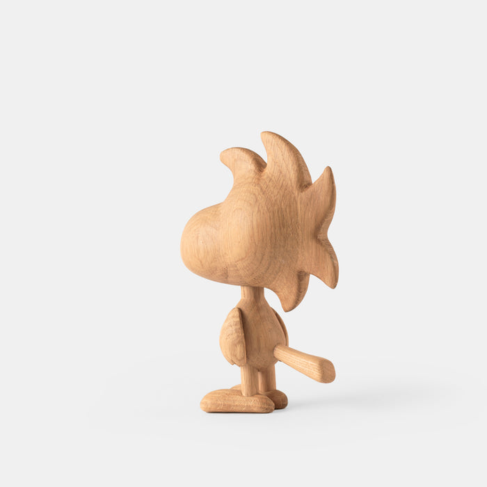 Wooden figurine of an animated cartoon character carved from light oak, featuring a rounded head with stylized protruding shapes, simplified body and tail, visible natural wood grain, and a smooth matte surface on a plain white background.