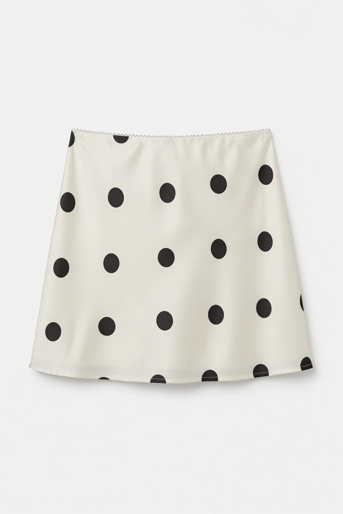 An A-line mini skirt in cream with a black polka dot pattern, displayed flat against a light gray background.
