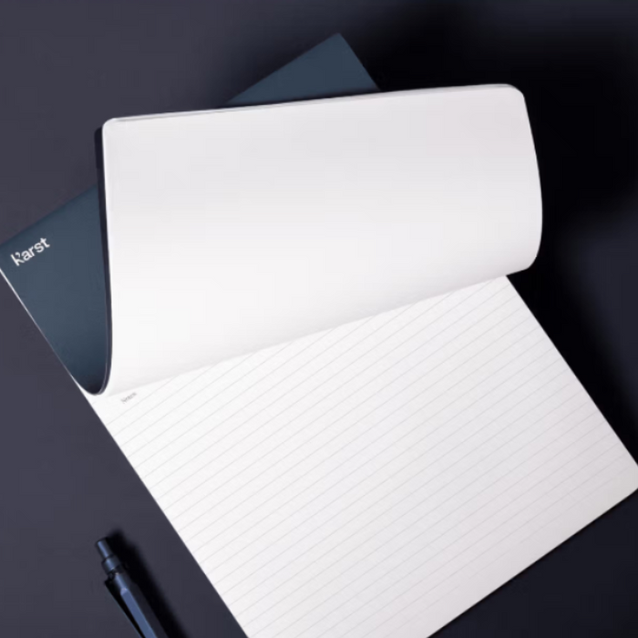 White notebook with a pen on a dark surface