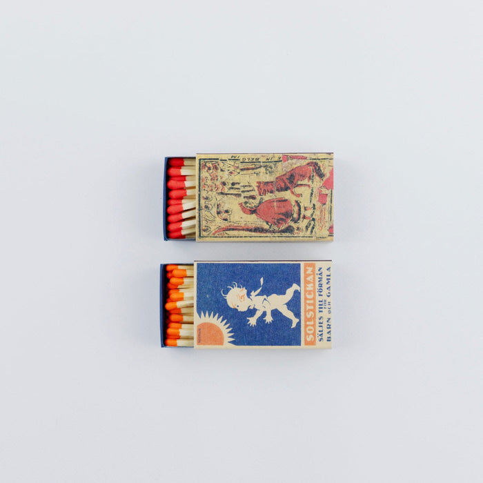 Two open vintage-style matchboxes arranged vertically on a white background. The top box shows red-tipped matches and an aged illustration with animals and figures, while the bottom box reveals orange-tipped matches and a blue label featuring a playful child-like figure, a sun motif, and retro typography.