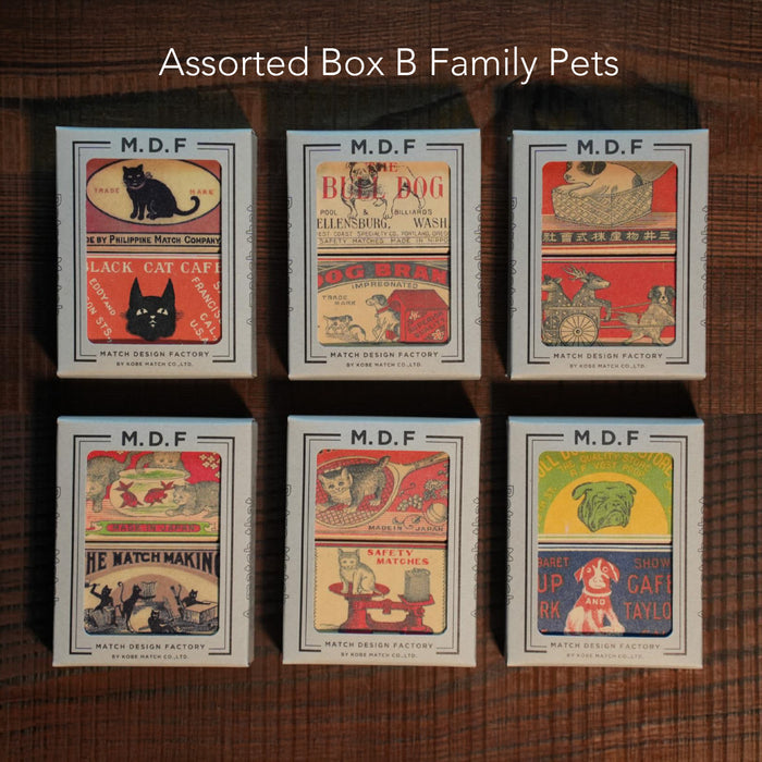 Six vintage-style matchboxes arranged in two rows of three on a wooden surface, labeled “Assorted Box B Family Pets.” Each M.D.F. Match Design Factory box features colorful retro illustrations of cats and dogs, including playful pets, café scenes, and classic animal-themed designs.