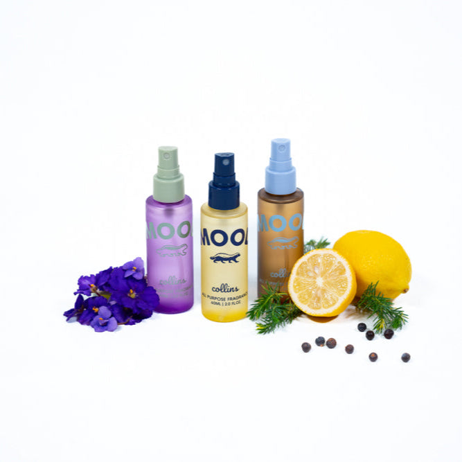 Three Mood Water all-purpose fragrance sprays displayed with flowers, lemon, juniper berries, and greenery, showcasing colorful water-based room and fabric scents on a clean white background.