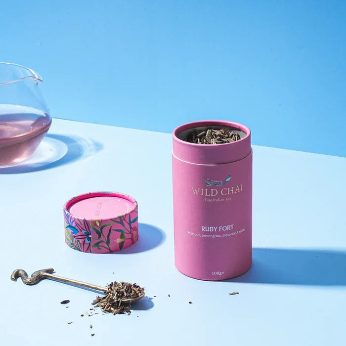 Pink tea canister labeled 'Wild Chai' with tea leaves on a blue background
