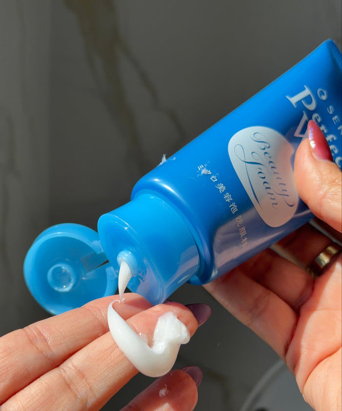 Person applying a white cream to their finger using a blue tube labeled 'Perfect Beauty'.