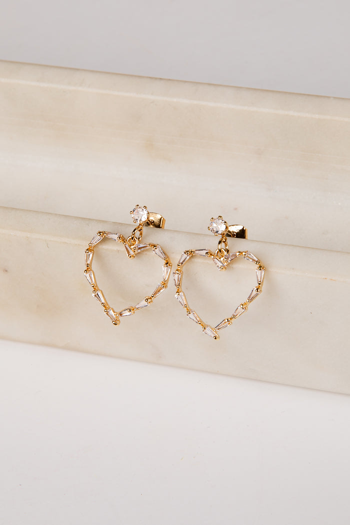 Gold heart-shaped earrings on a light wooden surface