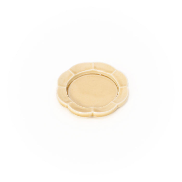 A single small ceramic dish on a white background with a scalloped edge and smooth, warm cream glaze, shown from above.