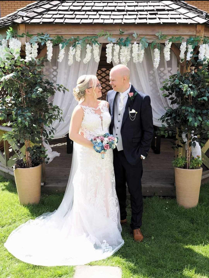 Groom wearing the Ivory Pocket Square - Snowdrop Handkerchief at a wedding, styled in a black suit with matching boutonnière under a floral gazebo.