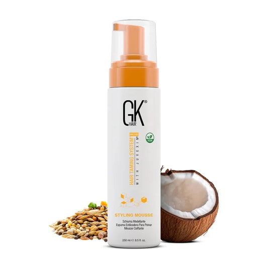 GK Hair Styling Mousse 250 ml white bottle with orange pump and vegan badge, beside a halved coconut and mixed seeds