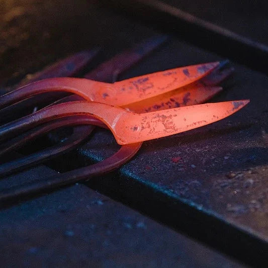 A close-up of glowing hot metal tools or bars resting on a dark workbench, with one piece illuminated in bright orange-red heat.