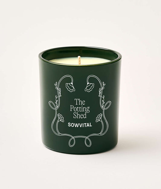 Green candle in a decorative container with 'The Potting Shed' branding on a white background