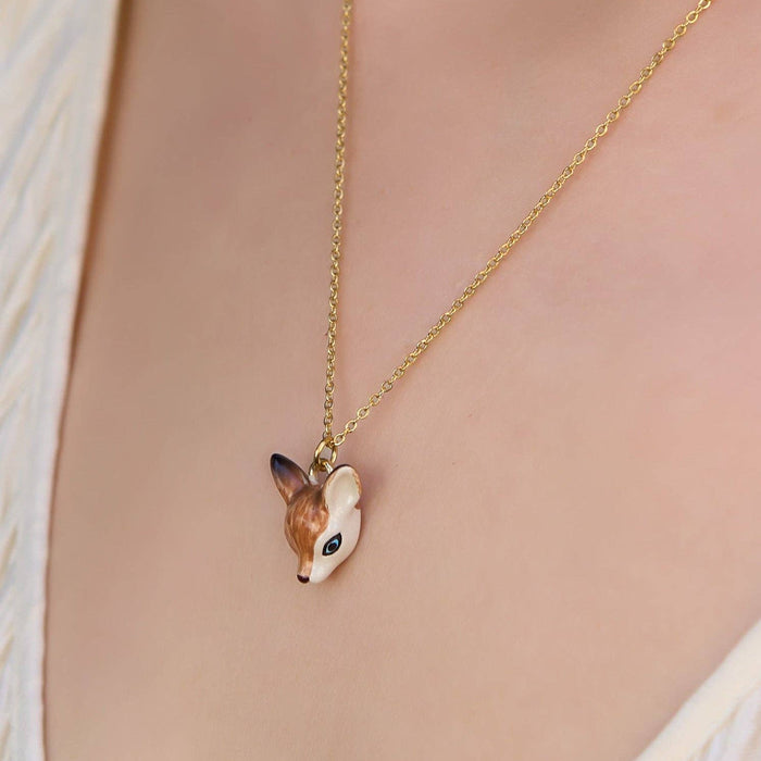 A gold chain necklace with a small deer head pendant, worn on a model's neck over a cream-colored textured top.