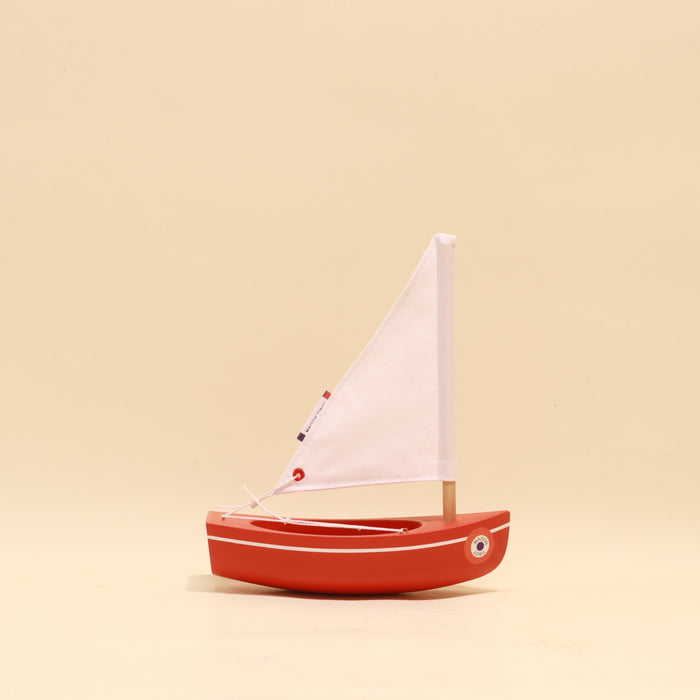 Small red sailboat with a white sail on a beige background
