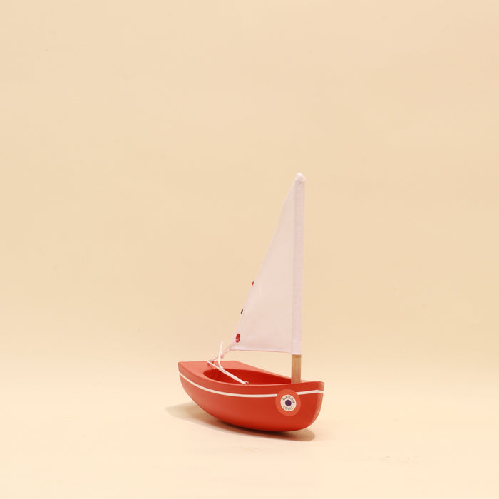 Small red toy sailboat with a white sail on a beige background