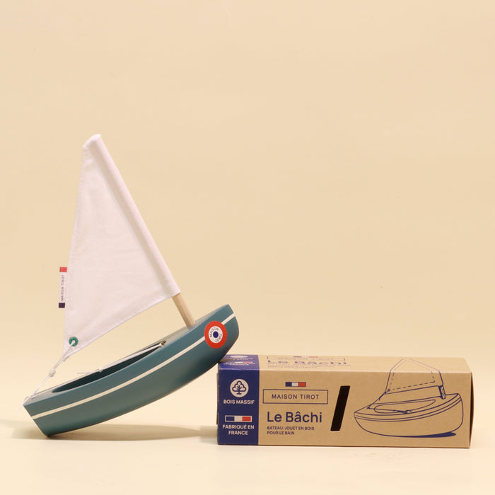 Toy sailboat with a white sail and blue body next to its packaging box on a beige background
