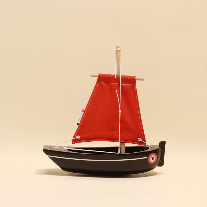 Model sailboat with a red sail on a beige background