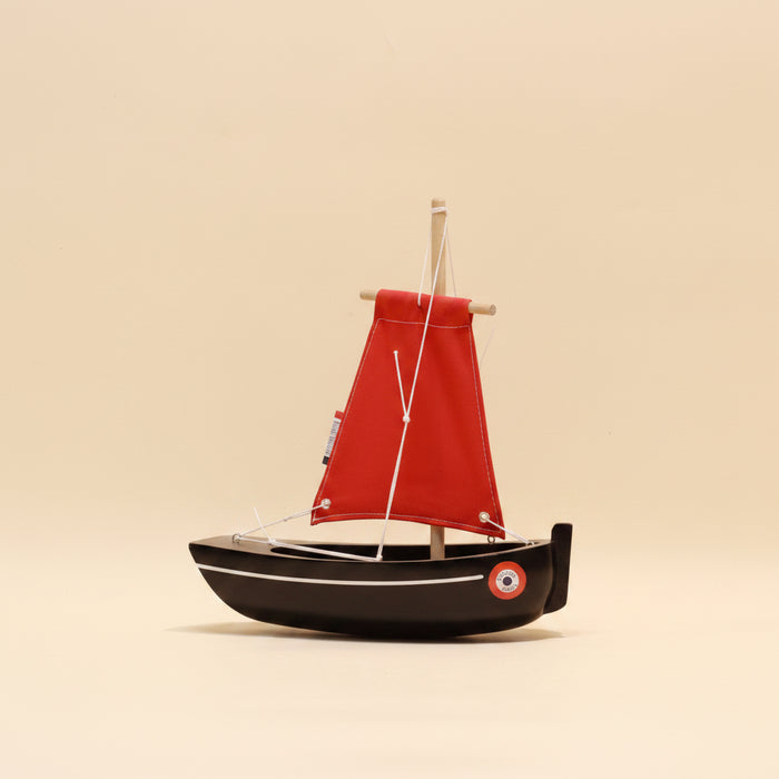 Model sailboat with a red sail on a beige background