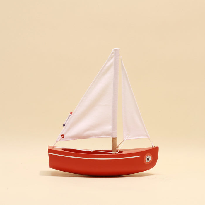 Red toy sailboat with white sails on a beige background