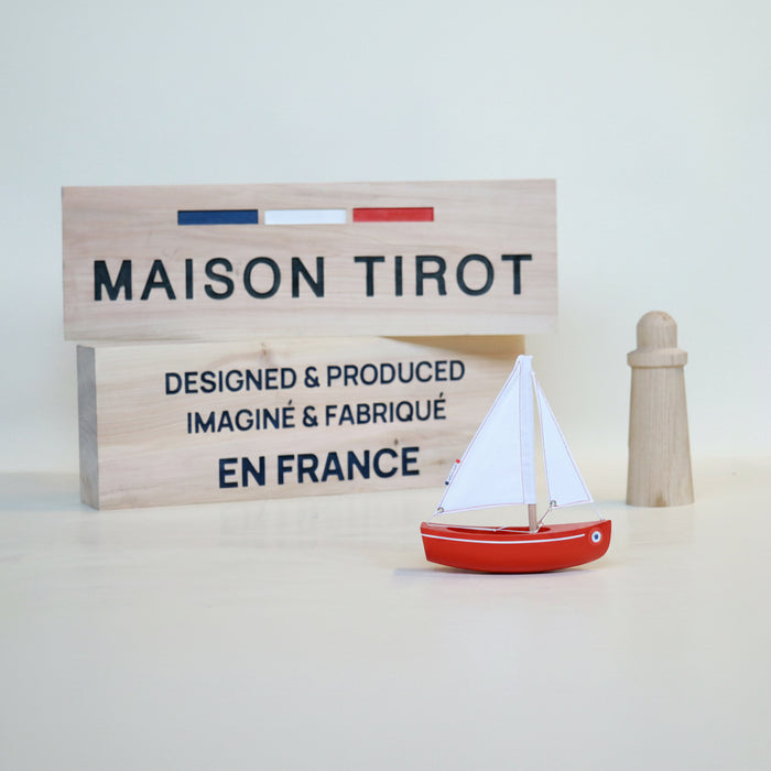 Red sailboat model with a wooden sign displaying 'MAISON TIROT' on a light background