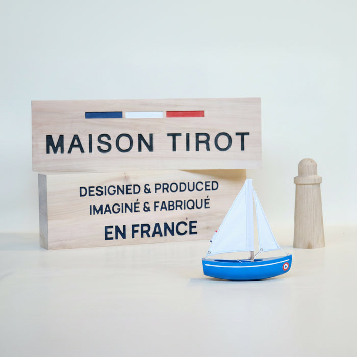 Model sailboat and wooden sign with 'MAISON TIROT' branding on a light background