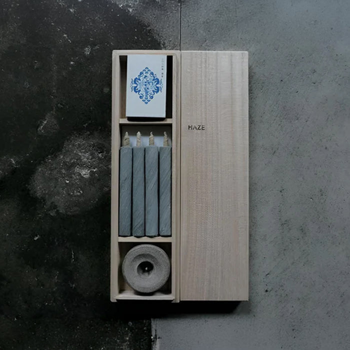 HAZE wooden gift box with four gray mini taper candles, a stone candle holder, and printed insert card, displayed on a dark textured surface in a minimalist product presentation.