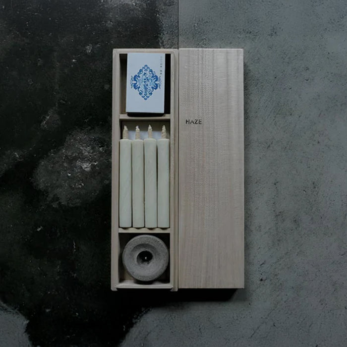 HAZE wooden gift box with four white mini taper candles, a stone candle holder, and printed insert card, displayed on a dark textured surface in a minimalist product presentation.