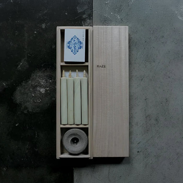 HAZE wooden gift box with four pale green mini taper candles, a stone candle holder, and printed insert card, displayed on a dark textured surface in a minimalist product presentation.