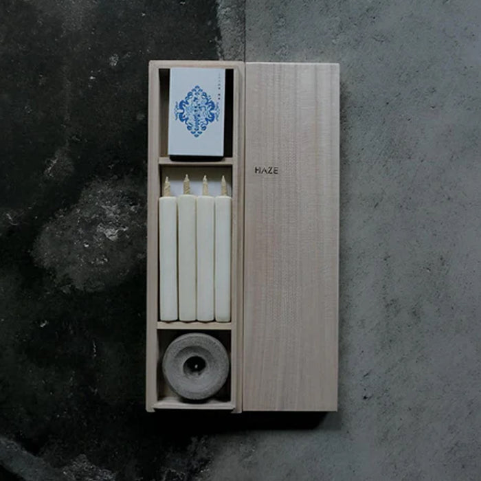 HAZE wooden gift box with four white mini taper candles, a stone candle holder, and printed insert card, displayed on a dark textured surface in a minimalist product presentation.