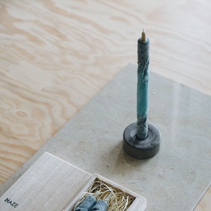 Blue and gray marbled taper candle in a stone candle holder, styled beside an open HAZE wooden gift box on a neutral stone and wood surface in a minimalist product presentation.
