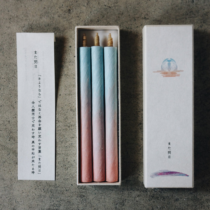 Set of three pastel blue and pink taper candles in an open presentation box with printed insert card, styled on a concrete surface in a minimalist art-inspired product display.