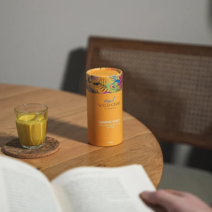 Orange 'Wild Chai' tea canister with a glass of yellow liquid on a wooden table.
