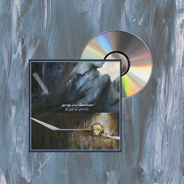 A CD by Young And Heartless, partly in its case, rests on a blue and gray painted background. Its cover shows abstract brushstrokes, a yellow dog’s face below, and white handwritten text at the center referencing Pull Of Gravity tracks.